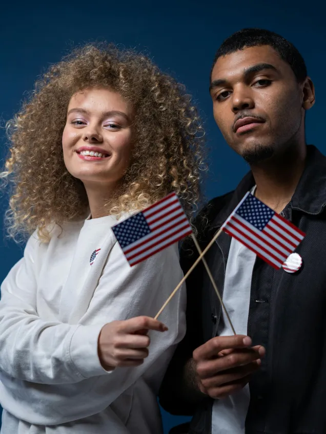 A young woman and man holding small American flags in front of a dark blue background
